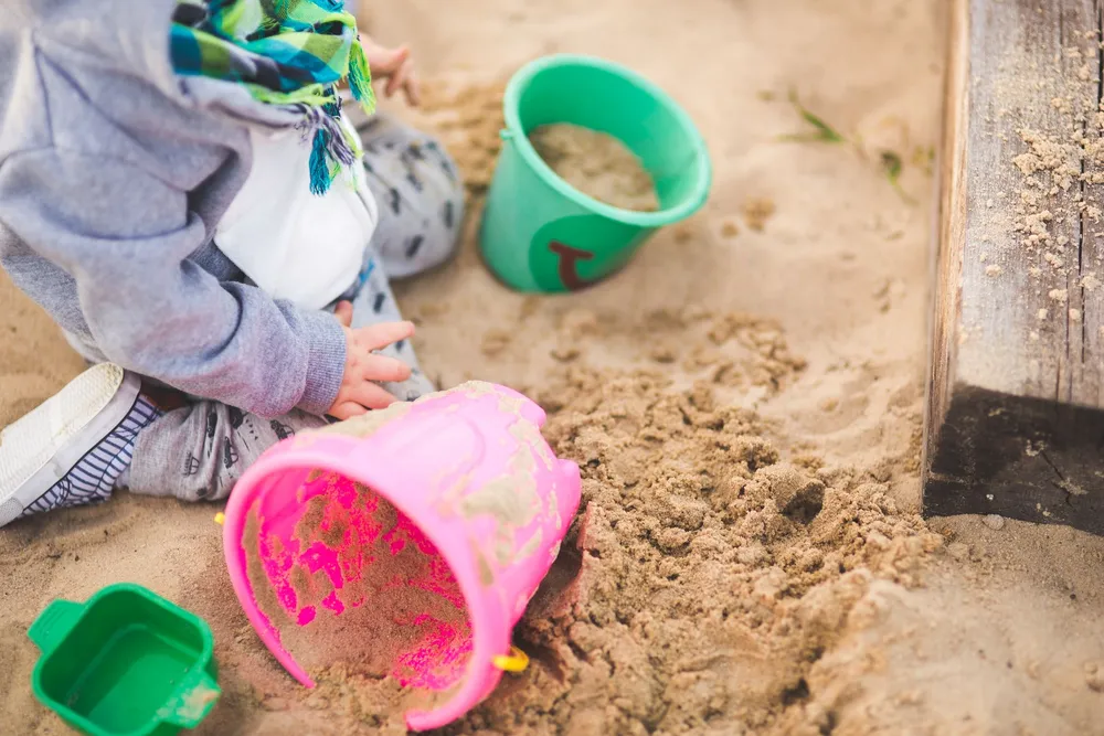 Child scooping clean play sand with buckets in a backyard sandbox