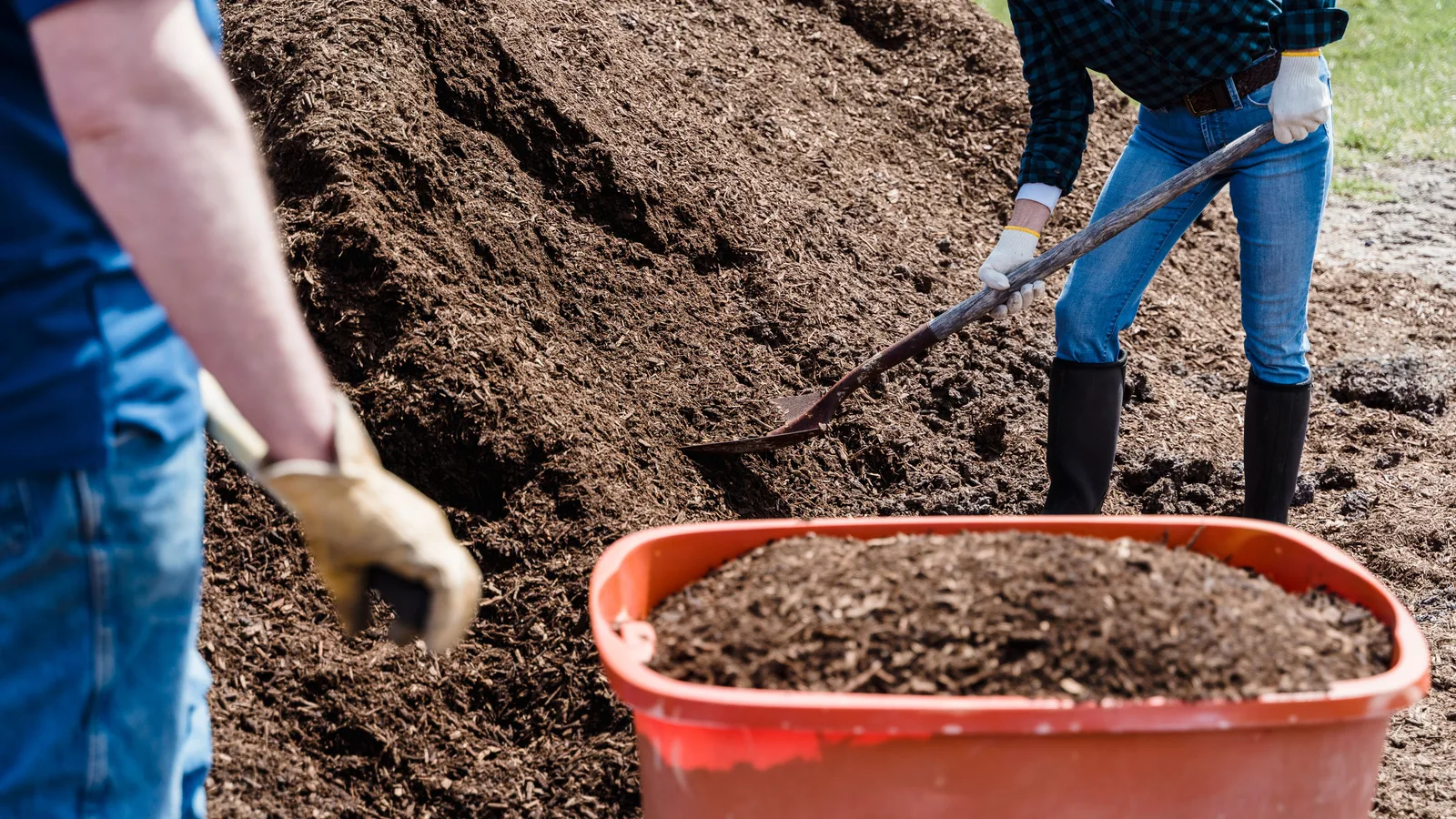 Shoveling a load of bulk mulch into a wheelbarrow to measure out cubic yards